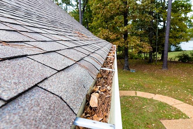 a person using a ladder to clean out leaves and debris from a rain gutter